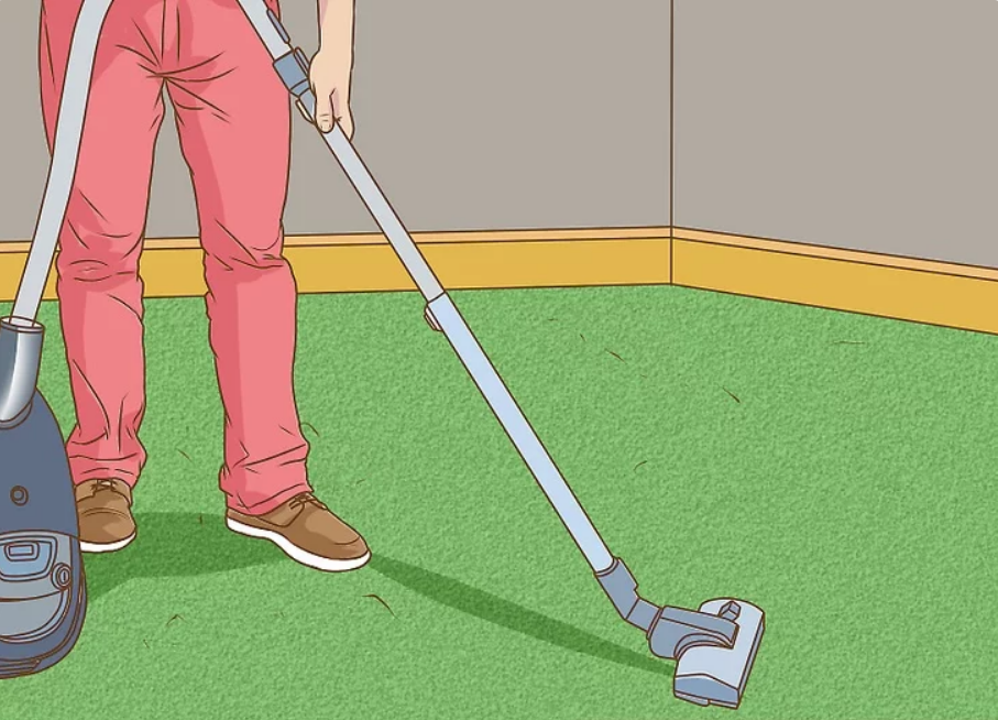 A man is cleaning a green carpet with a vacuum cleaner.